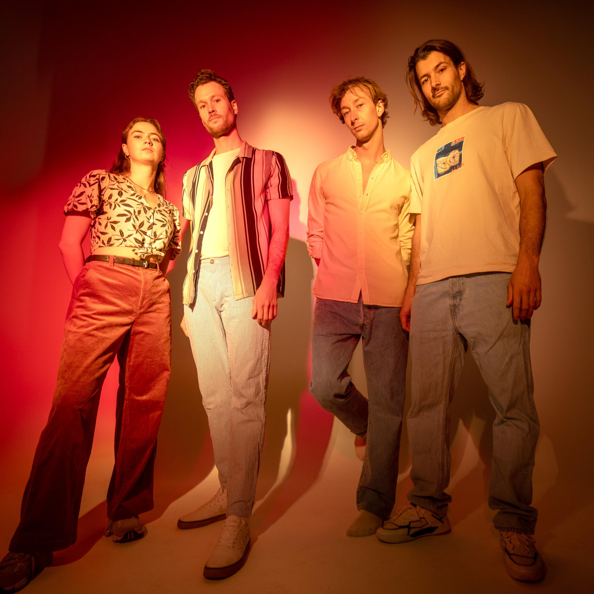 The four members of The Kiffs standing side by side against a wall lit in red and warm yellow light.